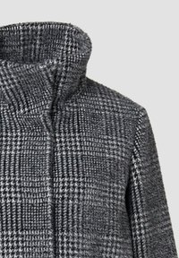 Szary płaszcz w wzór z wysokim kołnierzem, wykonany z teksturowanej tkaniny i kontrastujących czarno-białych krat. Płaska, strukturalna konstrukcja.