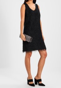 Svart ärmlös klänning med en texturerad, fluffig yta. Matchad med en silvrig kuvertväska och svarta klackskor med blockhäl och remmar.