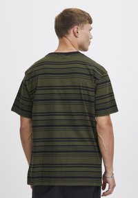 Camiseta a rayas verdes con rayas horizontales negras, de manga corta y cuello redondo. La tela parece suave y cómoda.