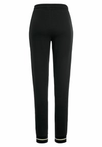 Schwarze Jogginghosen mit tailliertem Schnitt, elastischem Bund und gerippten Bündchen mit kontrastierenden weißen Streifen. Glatte Textur, minimalistischer Stil.