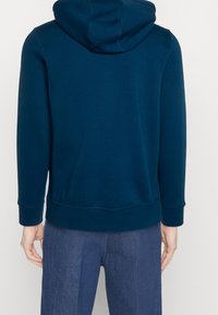 Felpa con cappuccio blu scuro in tessuto morbido, con cappuccio, maniche lunghe e polsini e orlo a coste. Vista posteriore con linee pulite e dettagli minimali.