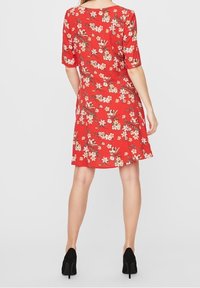Robe florale rouge à manches courtes, coupe évasée et tissu léger. Présente un motif floral dans des tons de rose et de vert.