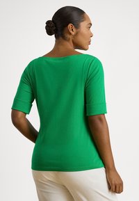 Πράσινη μπλούζα με φαρδιά λαιμόκοψη και κοντά μανίκια που είναι γυρισμένα. Λείο ύφασμα, εφαρμοστή γραμμή και απλός σχεδιασμός, κατάλληλη για καθημερινή χρήση.