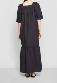 Robe maxi noire avec un décolleté carré et des manches courtes bouffantes. Couture de taille froncée menant à un bas évasé. Texture de tissu lisse.