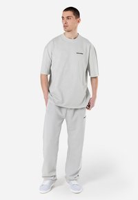 Hellgraues T-Shirt mit kurzen Ärmeln und Rundhalsausschnitt sowie einem kleinen Logo. Kombiniert mit passenden grauen Sweatpants und weißen Sneakern.