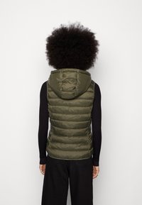 Gilet en duvet vert olive avec une capuche, présentant un design matelassé, une fermeture éclair et des manches longues noires côtelées en dessous.