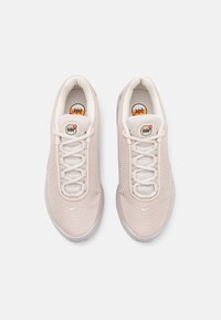 Paire de baskets Nike Air Max beige clair avec texture en mesh, logos swoosh blancs et lacets blancs, vues de dessus sur fond blanc.