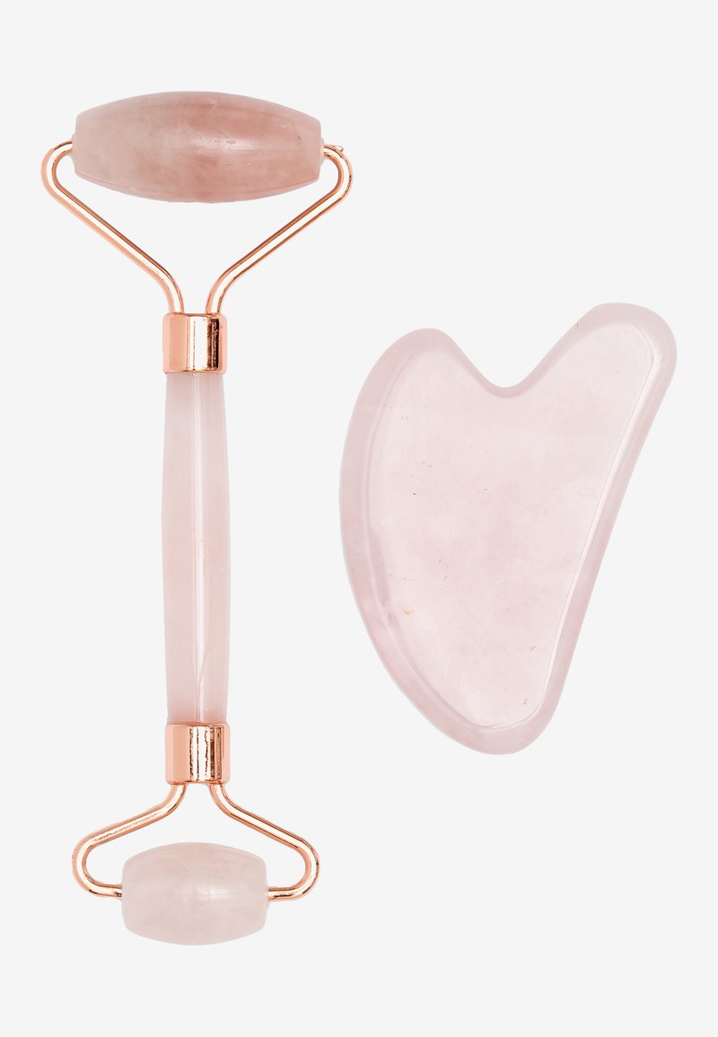 Rouleau de jade en quartz rose avec un dessus lisse et ovale et une poignée effilée, accompagné d'un outil gua sha en forme de cœur, tous deux avec des accents dorés.