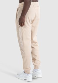 Beige sweatpants van textiel met een gestructureerde stof, elastische tailleband, zijzakken en subtiele paneelaccenten. Gecombineerd met witte sneakers.