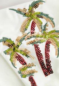 Embellished fabric featuring colorful sequined palm trees in green, gold, and red on a white background with textured stitching.
