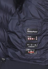 Interno di un giubbotto puff navy, con etichette per la cura dei tessuti, inclusi loghi e icone per impermeabilità, elasticità e caratteristiche di isolamento.