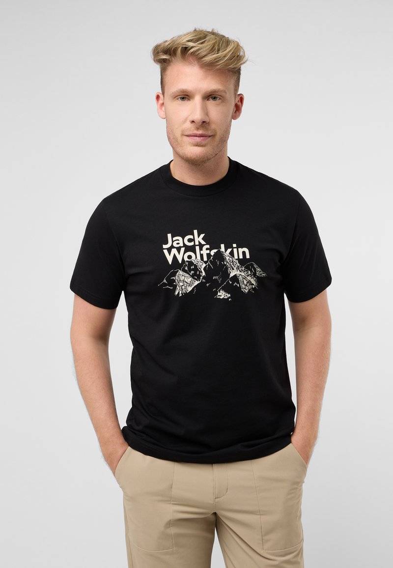 Schwarzes Baumwoll-T-Shirt mit einem weißen Grafikmotiv von Bergen und dem Text "Jack Wolfskin" in einer fetten Schriftart, Kurzarm und Rundhalsausschnitt.