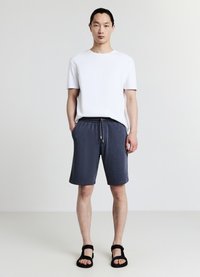 T-shirt blanc à manches courtes associé à un short bleu marine à cordon de serrage. Le short comporte des poches latérales et une coupe décontractée. Des sandales noires complètent la tenue.