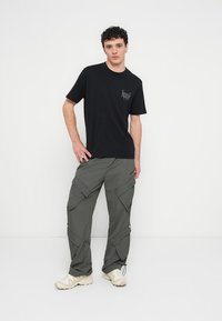 Black short-sleeve t-shirt with logo detail, paired with light gray cargo pants featuring multiple pockets and drawstring cuffs. Beige sneakers.