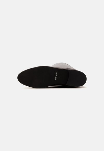 Semelle d'une botte de couleur claire couchée sur le côté avec une semelle noire, taille 37, et "Made in Italy" imprimé en bas.