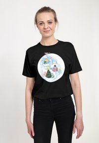 Camiseta de algodón negra con un gráfico circular y colorido de una escena invernal que incluye un castillo, un árbol de Navidad y personajes, todo ello sobre un fondo claro.