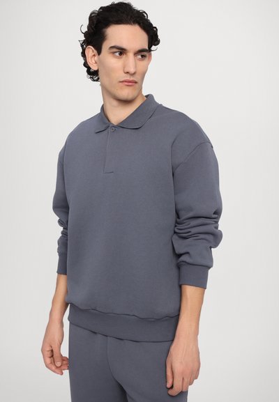 Šedá bavlněná mikina s polo límcem, žebrovanými manžetami a pasem. Má volný střih a hladkou texturu.