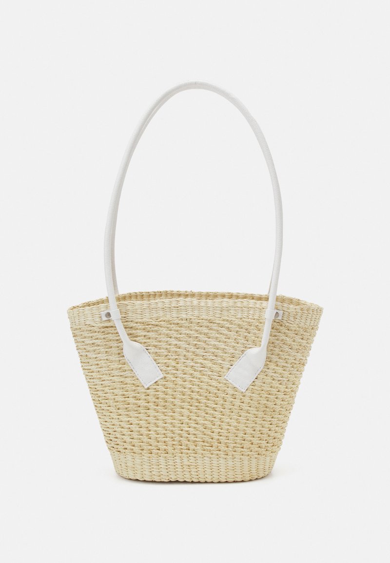 Woven straw tote bag in natural beige with a wide, flat base and white fabric handles. Features triangular white leather accents.