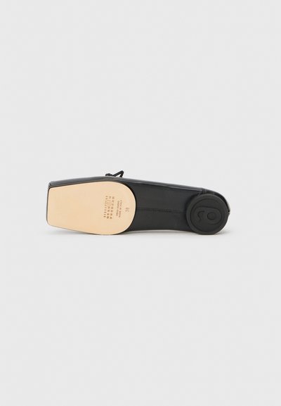 Chaussure en cuir noir au design épuré, avec un dessous doré et un talon en caoutchouc rond. Coutures visibles le long des côtés.