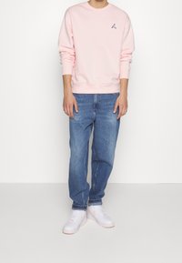 Sudadera de color rosa claro con puños y dobladillo acanalados, con un pequeño logo oscuro. Combinada con unos vaqueros de corte holgado azul y zapatillas blancas con detalles en rosa.