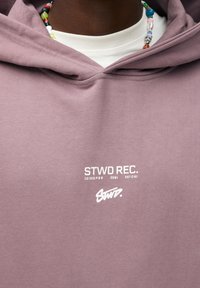 Lila Kapuzenpullover aus Baumwolle mit einem weißen Logoaufdruck auf der Vorderseite. Enthält strukturiertes Material und eine Kapuze mit Kordelzug.