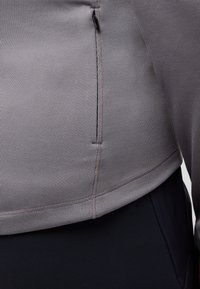 Top in tessuto grigio a righe con dettagli di zip laterale, sopra un cinturino scuro, che mette in evidenza un design aderente e moderno.