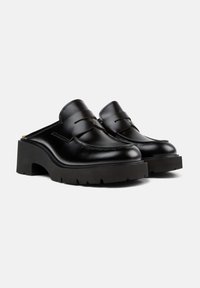Mule in pelle nera con suola spessa e scanalata, caratterizzate da un classico design penny loafer e dettagli cuciti sulla tomaia.