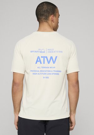 Man met de rug naar de kijker, draagt een wit shirt met korte mouwen met blauwe tekst: "ATW All Terrain Wear Physical Education & Training."