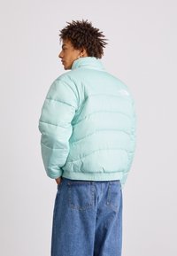 Giacca puffer verde menta con design trapuntato, vita elasticizzata, colletto alto. Logo presente sul retro, abbinata a pantaloni in denim blu.
