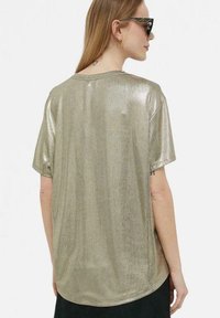 T-shirt metallizzato oro a maniche corte con vestibilità ampia, superficie testurizzata e orlo arrotondato, vista da dietro.