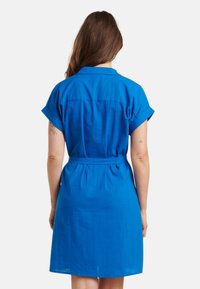 Korte mouwen, kraagjurk van levendig blauwe stof. Bevat een ceinture taille en een lichtjes uitlopende rok. Soepele textuur met minimale details.