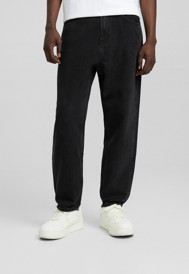 Jeans de mezclilla negra con corte recto, con bolsillos laterales y costuras sutiles. Combinados con zapatillas blancas.