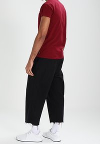 Camiseta de algodón roja, de mangas cortas, combinada con pantalones negros de corte holgado. Zapatillas deportivas blancas y calcetines blancos visibles, diseño minimalista en general.