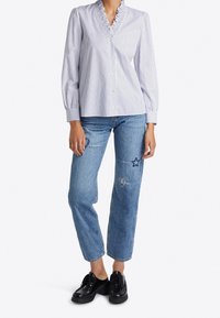 Gestreifte Bluse mit Rüschekragen, kombiniert mit ausgewaschenen Jeans, die mit gestickten Sternen und Herzen verziert sind, getragen mit schwarzen Schuhen.