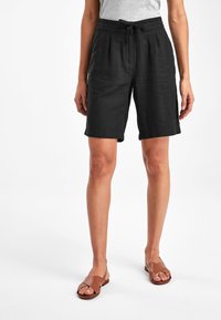 Zwarte linnen shorts met een taillekoord, plooiën en zijzakken, gecombineerd met bruine platte sandalen. Gladde textuur met een losse pasvorm.