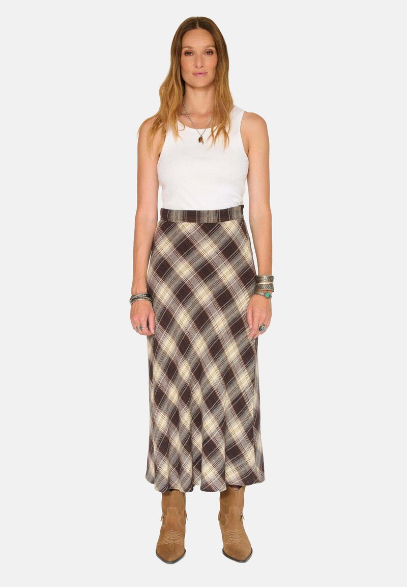 Jupe maxi à carreaux dans des tons de marron, crème et beige avec une taille ajustée. Associée à un débardeur blanc et des bottines marron.