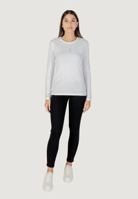Maglia bianca a maniche lunghe con scollatura rotonda, caratterizzata da una piccola stampa sul petto. Abbinata a legging neri e sneakers bianche.