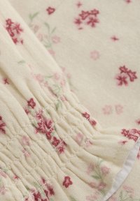 Blomster mønstrede stof i creme med små lyserøde og røde blomster. Har en samlet tekstur med elastiske detaljer og en let, struktureret vævning.