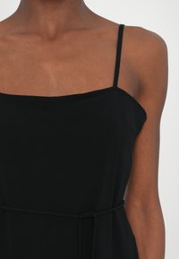 Black sleeveless dress with thin straps, featuring a fitted bodice and a tied belt at the waist. Smooth fabric with a matte texture.