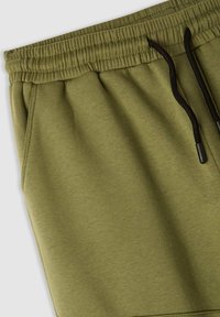 Oliwkowe spodnie dresowe z prążkowanym paskiem w talii, sznurkiem do wiązania oraz miękkim, gładkim materiałem z widocznymi przeszyciami.