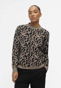 Pull beige avec un imprimé léopard noir, col rond, manches longues et poignets côtelés. Matière en maille douce avec une coupe décontractée.