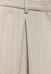 Pantalon beige à fines rayures verticales, avec une ceinture et des plis. Le tissu a une texture lisse et un design ajusté.