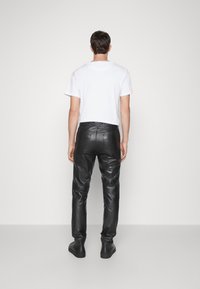 Svarta läderbyxor med en åtsittande design, med subtila sömnadsdetaljer. Kombineras med en enkel vit t-shirt med kort ärm.