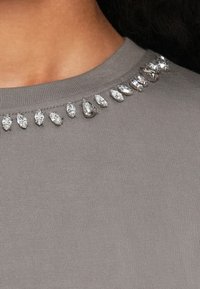 Grå ribbestrikket topp med rund halsringning, pyntet med klare, dråpeformede rhinestones langs kragen.
