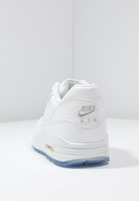 Vita Nike Air sneakers med strukturerad ovandel, grå logotyp på hälen, vadderad krage och genomskinlig blå sula. Ren, minimalistisk design.