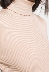 Pull en maille côtelée beige clair à col roulé, avec une coupe près du corps et une texture douce, ornée de subtiles rayures horizontales sur la surface.