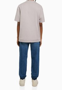 Light gray short-sleeve shirt with a relaxed fit, paired with blue jogger-style pants. Pants have elastic cuffs and a casual design.