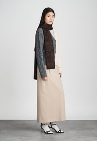 Grå og creme kabelstrikket cardigan med brun tørklæde med logo, beige maxiskirt og sorte strophæle med ankelaccentuer.