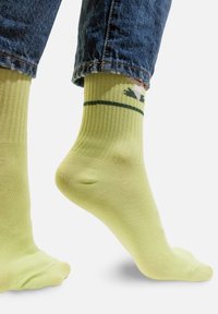 Zielone prążkowane skarpetki o gładkiej fakturze, z małym wzorem z motywem roślinnym w ciemniejszym zielonym i białym kolorze blisko mankietu.