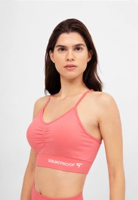 Sportivo rosa con design arricciato, spalline regolabili e una banda elastica con logo. Tessuto liscio con una silhouette aderente.